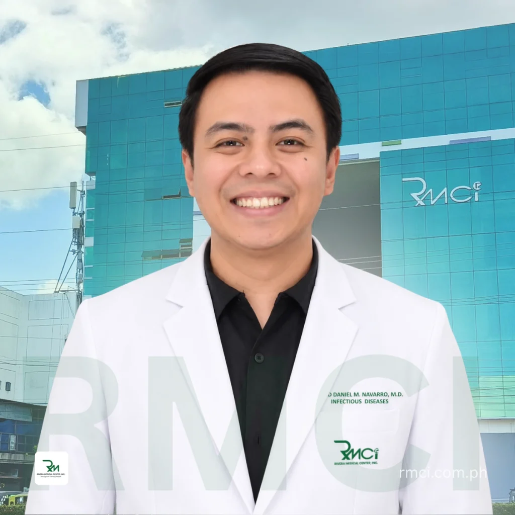 Smiling doctor in a white lab coat posing in front of a blue RMCI building.