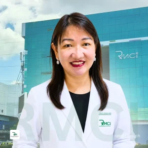 Smiling female doctor in a white coat outside a blue glass RMCI building with logo point of context clarity