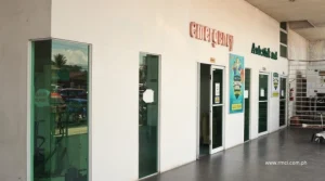 Exterior walkway of a medical clinic with an emergency entrance, glass doors, and posters along the wall on a tiled hallway